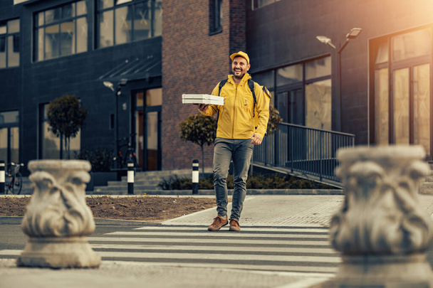 Courrier en uniforme jaune avec une boîte de livraison à l'arrière.Homme livraison pizza au client. - Photo, image