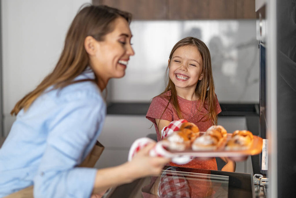 Vonzó anya és az aranyos kislánya együtt csinálnak muffint a konyhában. Élvezik az együtt töltött időt.. - Fotó, kép