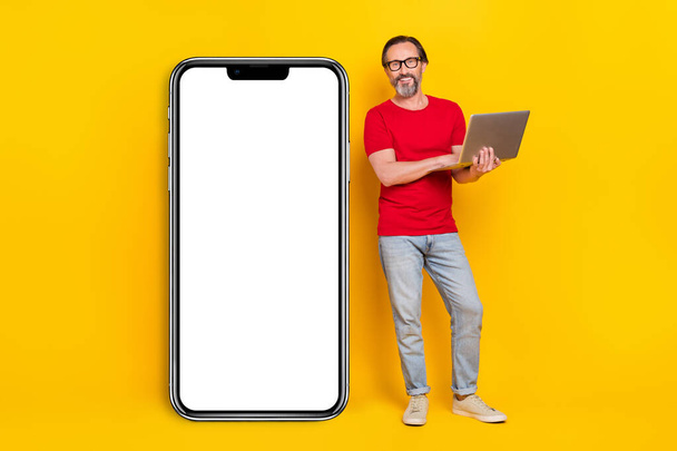 Photo of sweet cute guy pensioner dressed red t-shirt glasses typing gadget empty space isolated yellow color background. - Photo, image