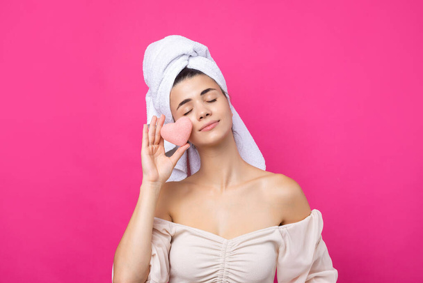 Hermosa chica atractiva alegre con una toalla en la cabeza, sostiene una esponja en forma de corazón rosa. - Foto, Imagen