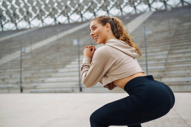 Sports woman in sportswear does exercises outdoors. Young woman doing stretching exercise. Sport, active lifestyle, healthy lifestyle concept. - Foto, Imagen