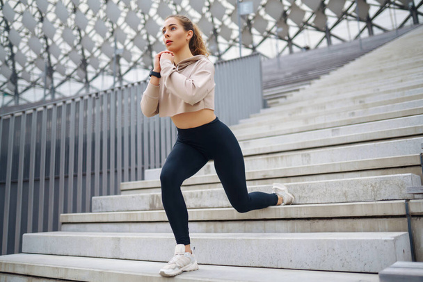 Sports woman in sportswear does exercises outdoors. Young woman doing stretching exercise. Sport, active lifestyle, healthy lifestyle concept. - Fotografie, Obrázek