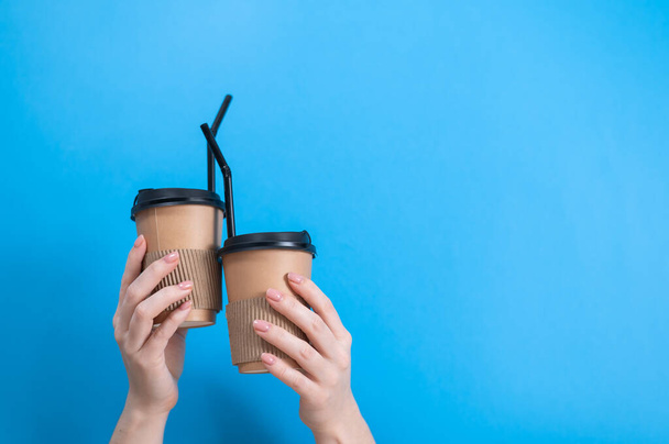 A woman holds two cardboard cups with coffee on a blue background - Foto, afbeelding