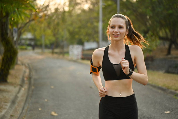 Sporty young woman jogging in the park at evening with sunset. Sport and healthy lifestyle concept. - Photo, Image