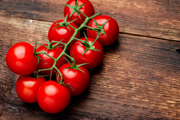 Branch of fresh cherry tomatoes on a brown wooden background. - 写真・画像