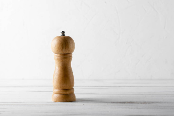 Wooden pepper shaker grinder on a white wooden background. - Zdjęcie, obraz