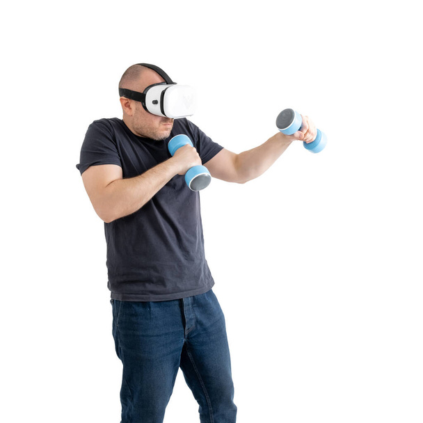 Unsportsmanlike middle-aged man wearing virtual reality glasses with dumbbells. Isolated on a white background. - Foto, afbeelding