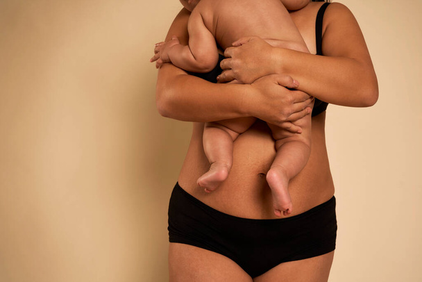 Неузнаваемая женщина в нижнем белье держит малыша - Фото, изображение
