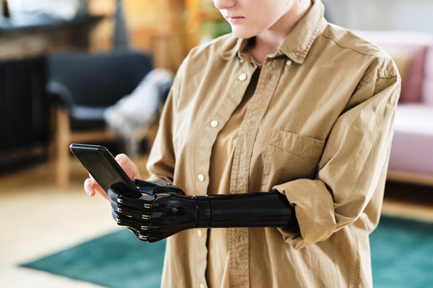 Primo piano della giovane donna in camicia con braccio protesico che impara ad usare il suo smartphone - Foto, immagini