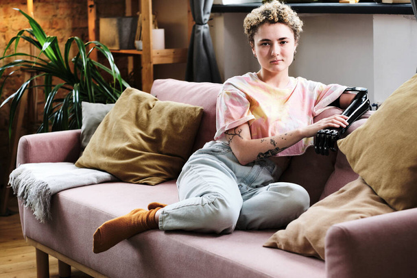 Oturma odasındaki kanepede oturan protez kollu genç kadının portresi. - Fotoğraf, Görsel