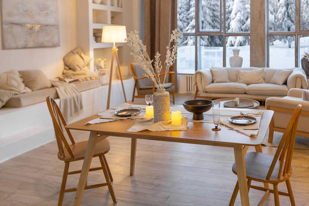 cozy warm home interior of a chic country chalet with a huge panoramic window overlooking the winter forest. open plan, wood decoration, warm colors and a family hearth - 写真・画像