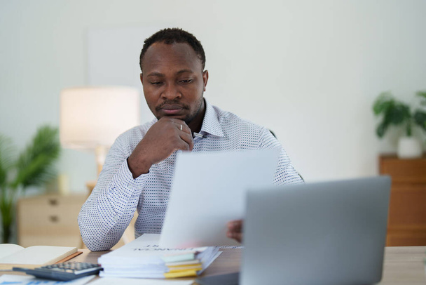 mężczyzna w średnim wieku Amerykanin African za pomocą laptopa komputerowego z planowaniem pracy nad dokumentem finansowym, podatkowym, giełdowym, księgowym i doradcą finansowym. - Zdjęcie, obraz