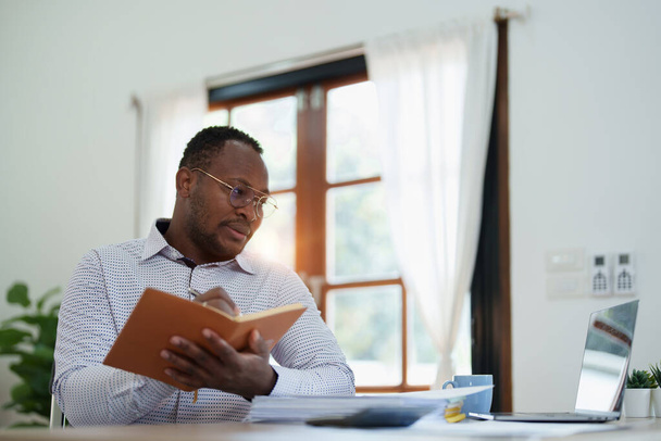 hombre de mediana edad americano africano utilizando ordenador portátil con la planificación de trabajo en documentos financieros, impuestos, intercambio, contabilidad y asesor financiero. - Foto, imagen