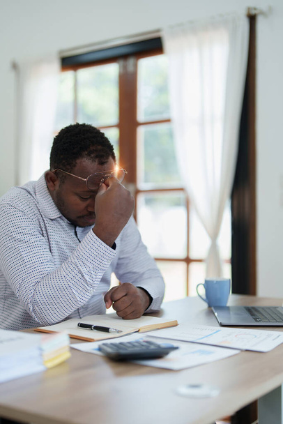 Burnout hombre de negocios africano americano en estrés trabaja con muchos documentos de papeleo, ataque de migraña, freelance, trabajo desde casa. - Foto, imagen