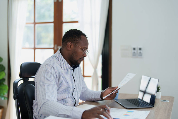 Μεσήλικας άνθρωπος Αμερικανός Αφρικής χρησιμοποιώντας αριθμομηχανή για τον υπολογισμό και φορητό υπολογιστή με το σχεδιασμό εργασίας σε οικονομικό έγγραφο, φόρο, ανταλλαγή, λογιστική και οικονομικός σύμβουλος. - Φωτογραφία, εικόνα
