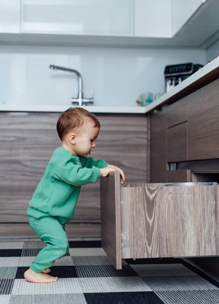 Little child exploring drawer in kitchen. Dangerous situation - Photo, Image