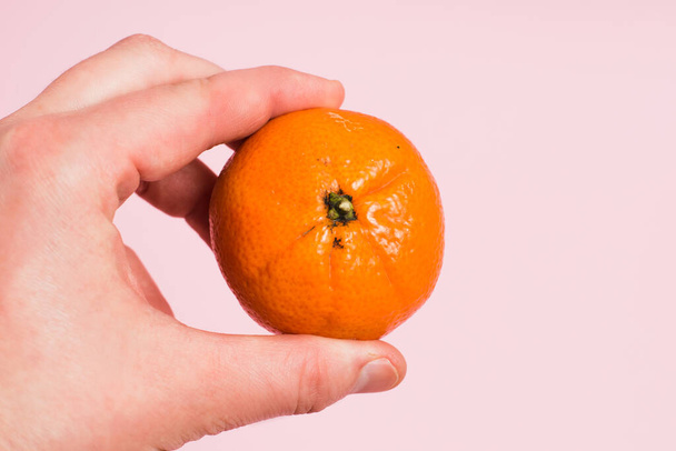 Tangerine in female hand on pink paper background with copy space - Φωτογραφία, εικόνα