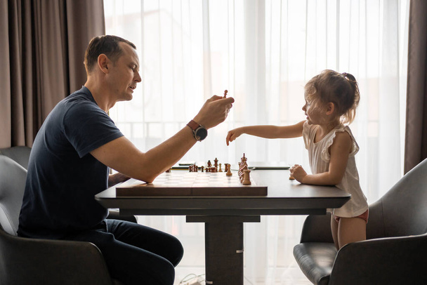Padre enseñando a su hija a jugar al ajedrez en la mesa de la cocina casera. El concepto de desarrollo y educación en la primera infancia. Ocio familiar, comunicación y recreación. Foto de alta calidad - Foto, Imagen