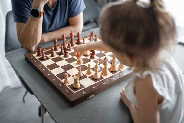 Küçük kız babasıyla ev mutfağında satranç oynuyor. Erken çocukluk gelişimi ve eğitim kavramı. Aile eğlencesi, iletişim ve eğlence. Yüksek kalite fotoğraf - Fotoğraf, Görsel