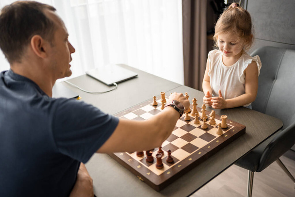 Père enseignant à sa petite fille à jouer aux échecs à la table dans la cuisine de la maison. Le concept développement de la petite enfance et l'éducation. Loisirs, communication et loisirs en famille. Photo de haute qualité - Photo, image