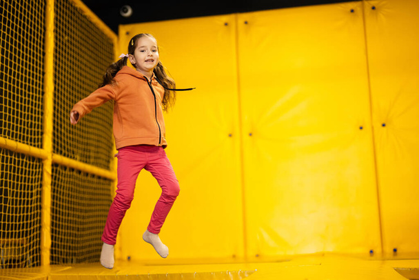 Little girl kid jumping on trampoline at yellow playground park. Child in motion during active entertaiments. - Fotó, kép