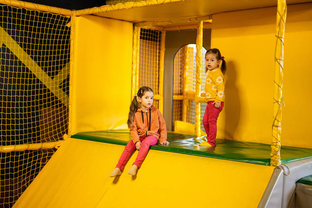 Siblings sliding at yellow playground park. Sisters in active entertaiments. - Foto, Bild
