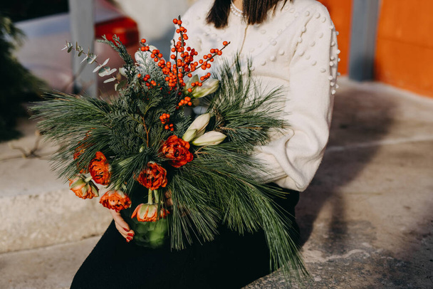 Woman holding a christmas bouquet made of red tulips, ilex berries, pine branches and amaryllis flowers. - Foto, immagini