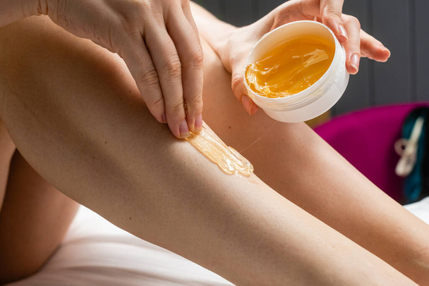 Uma jovem esbelta aplica pasta de açúcar para depilação de cabelo em suas pernas. Close-up. - Foto, Imagem