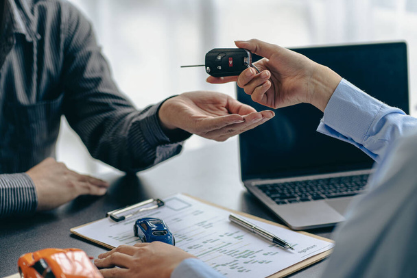 Explain promotions and car insurance for rental or purchase. A car dealer or sales manager hands the keys to the car owner and explains the terms of the car contract at a desk in the office. - Photo, Image