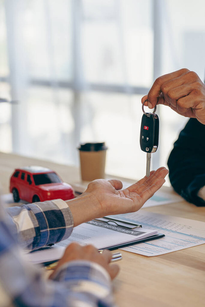 Explain promotions and car insurance for rental or purchase. A car dealer or sales manager hands the keys to the car owner and explains the terms of the car contract at a desk in the office. - Foto, Imagem