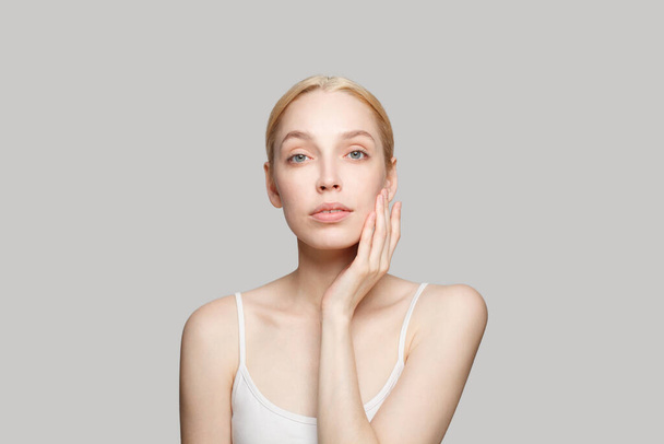 Портрет красивой женщины в белом топе, прикасающейся к щеке изолирован на сером фоне. Красота, косметика, кожа, гламур - Фото, изображение