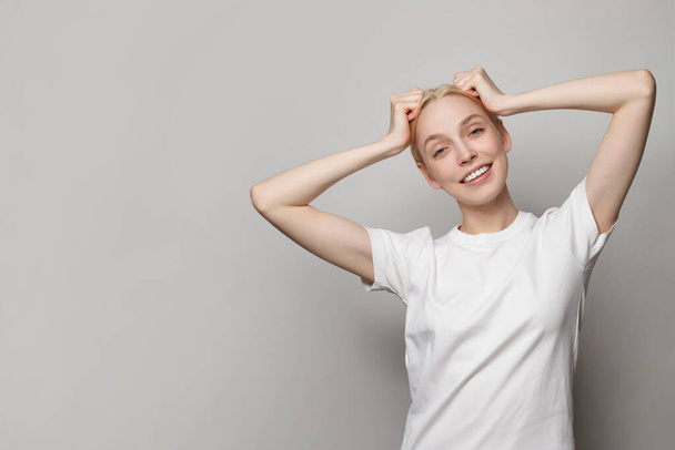 Joyful young woman wearing white empty t-shirt posing on grey studio background - Valokuva, kuva