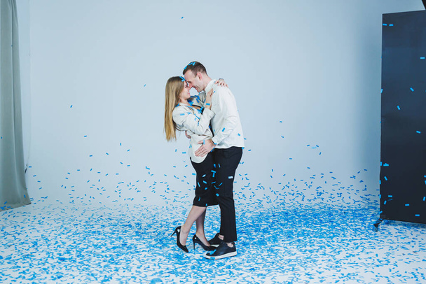 Young happy married couple hugging in blue confetti. A couple in love rejoices and has fun. Gender photo session - Foto, Imagem