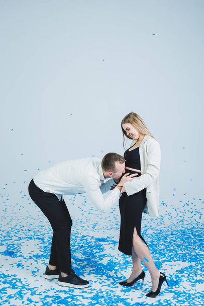 Młoda szczęśliwa para przytulająca się w niebieskim konfetti. Para zakochanych raduje się i bawi. Sesja zdjęciowa płci - Zdjęcie, obraz
