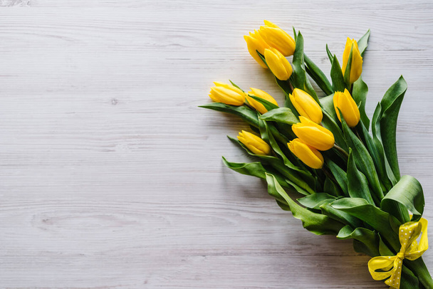 Bouquet of yellow tulips on white wooden background with space for message. Summer flowers concept. Spring. Holiday greeting card for Valentine's, Women's, Mother's Day, Easter. Top view, flat lay. - Foto, Imagem