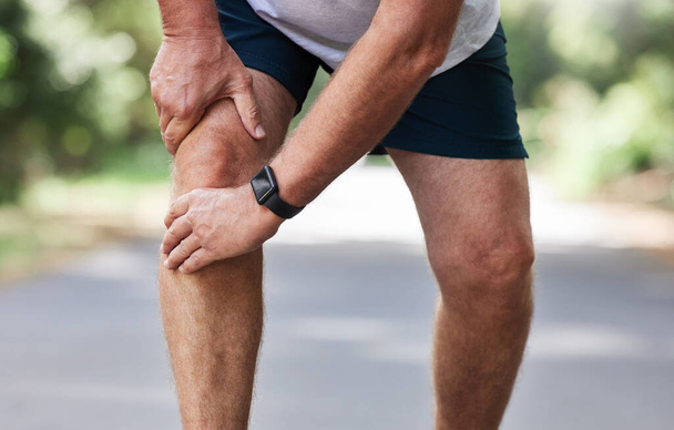 Running, knee pain and old man with hand on leg in park in for outdoor fitness and workout exercise. Health, wellness and muscle strain, senior runner with injury, hands on ache in support or relief - Photo, Image