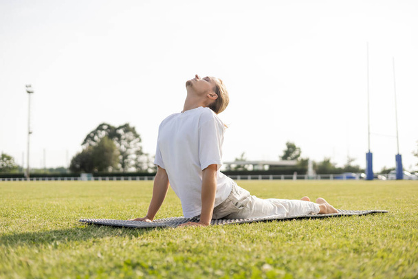 surface level of young yoga man practicing cobra pose with closed eyes on green grass outdoors - Foto, Imagem