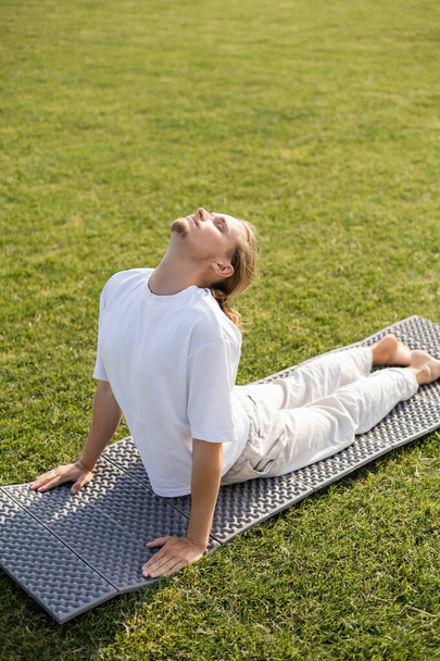 young bearded man with closed eyes meditating in cobra pose on yoga mat  - Photo, Image