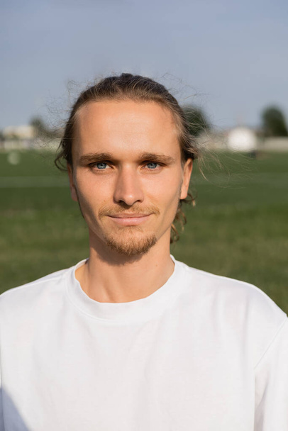retrato de jovem homem de ioga barbudo em t-shirt branca sorrindo para a câmera ao ar livre - Foto, Imagem