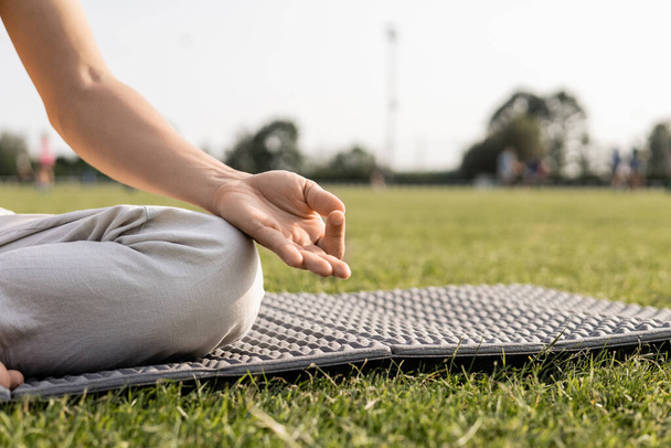 partial view of man meditating with gyan mudra gesture on yoga mat in green field - Foto, imagen