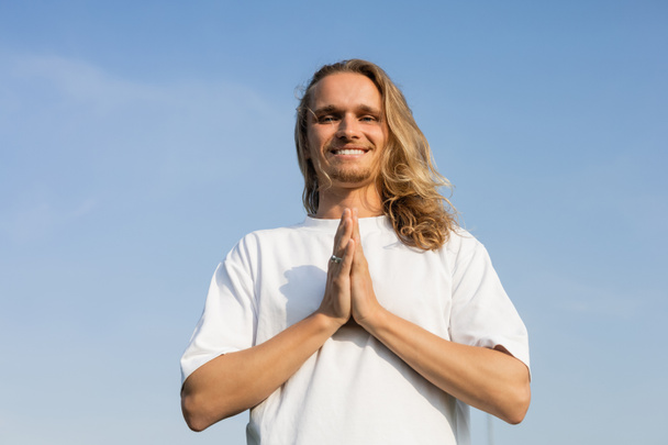 low angle view of carefree long haired man meditating with anjali mudra gesture against blue cloudless sky - Fotografie, Obrázek