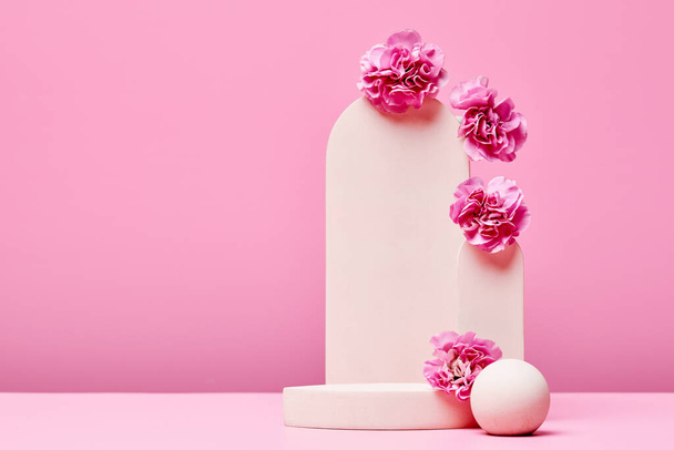 βάθρο με λουλούδια και κομψή καμάρα σε παστέλ ροζ φόντο. στάδιο για την παρουσίαση καλλυντικών ή προϊόντων ομορφιάς. minimal σχεδιασμός μόδας. αντίγραφο χώρου - Φωτογραφία, εικόνα