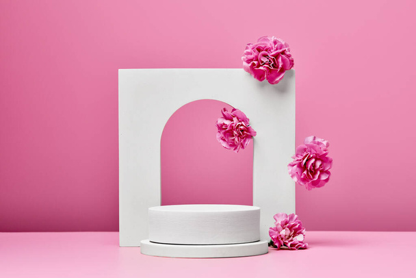 wit podium met roze bloemen en elegante boog geïsoleerd op pastel roze achtergrond. podium voor presentatie cosmetische producten - Foto, afbeelding
