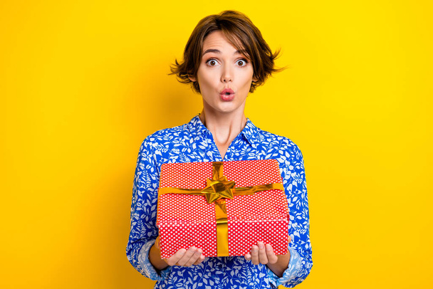 Photo of adorable impressed woman dressed blue blouse rising red present box isolated yellow color background. - Фото, изображение