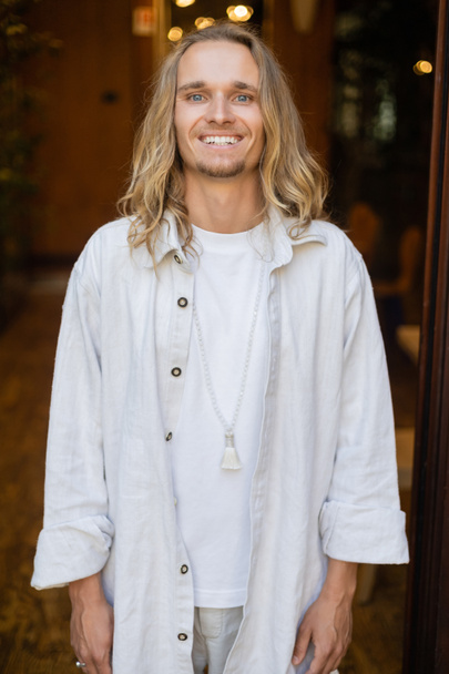 happy long haired yoga man in white cotton clothes and beads smiling at camera outdoors - Foto, afbeelding