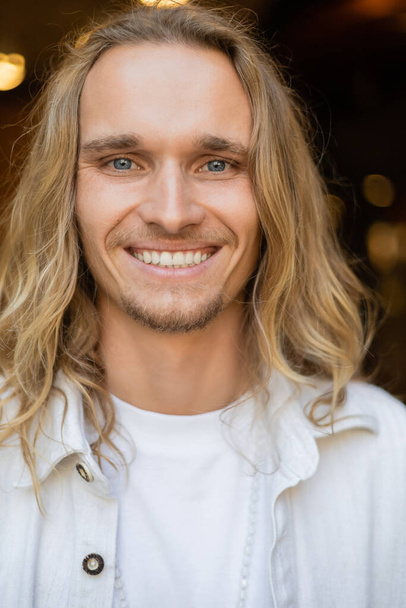 portrait de jeune homme de yoga insouciant avec de longs cheveux blonds regardant la caméra à l'extérieur - Photo, image