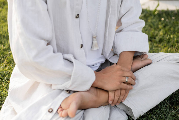 cropped view of man in white clothes sitting in lotus pose during meditation outdoors - Zdjęcie, obraz
