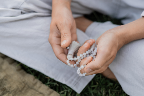 abgeschnittene Ansicht eines jungen Mannes, der Mala-Perlen hält, während er im Freien meditiert - Foto, Bild