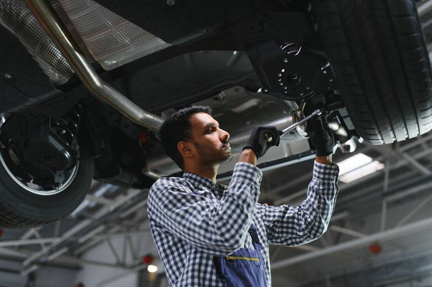 latin hispanic auto mechanic in uniform is examining a car while working in auto service. - Фото, зображення