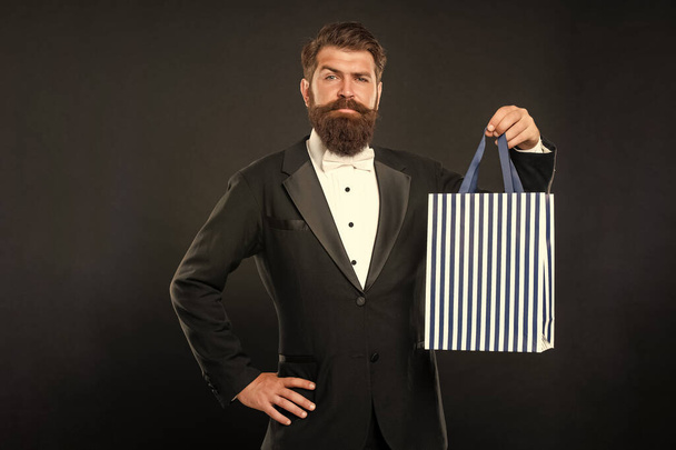smiling man in tuxedo bow tie formalwear on black background with business reward in shopping bag. occasion greeting. copy space. - Фото, зображення
